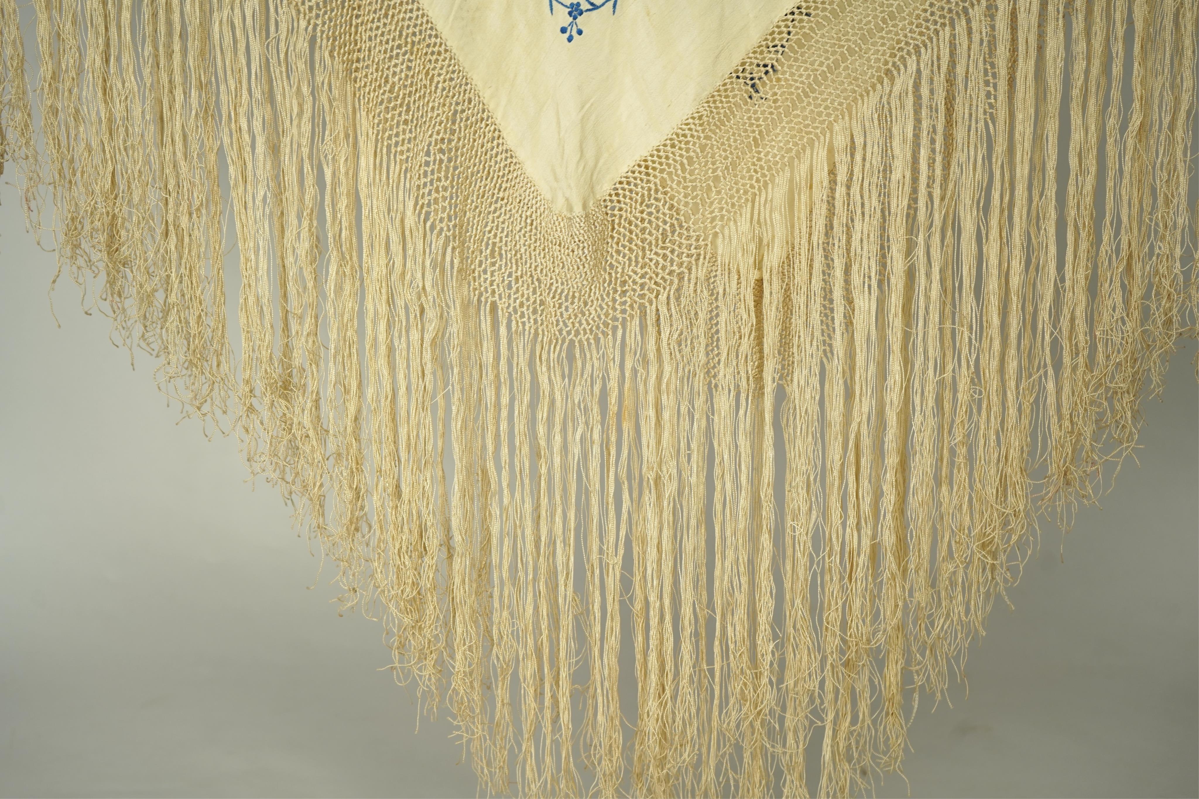 A Chinese cream silk polychrome embroidered shawl with a long fringe. Embroidered with four unusual corner cartouches of Pagoda, flowers, birds, cats and dogs. 132cm x 126cm.